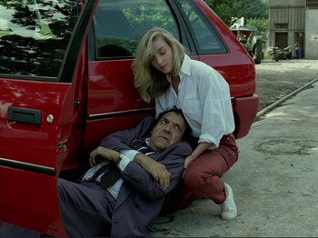 Movie still from “Oh, Woe Is Me” (1993), directed by Jean-Luc Godard – A woman standing next to a man laying on the ground next to a red car; Medium shot, High angle
