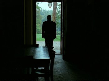 Movie still from “Oh, Woe Is Me” (1993), directed by Jean-Luc Godard – A man standing in front of an open door; Wide shot, Low angle