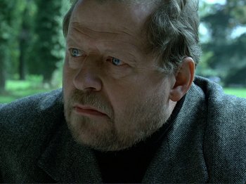 Movie still from “Oh, Woe Is Me” (1993), directed by Jean-Luc Godard – An older man with a beard and a jacket on; Close Up shot, Over the shoulder angle
