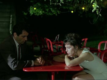 Movie still from “Oh, Woe Is Me” (1993), directed by Jean-Luc Godard – A man and a woman sitting at a red table; Medium shot, Over the shoulder angle