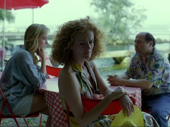 Movie still from “Oh, Woe Is Me” (1993), directed by Jean-Luc Godard – A woman sitting at a table in front of two other people; Medium shot, Over the shoulder angle