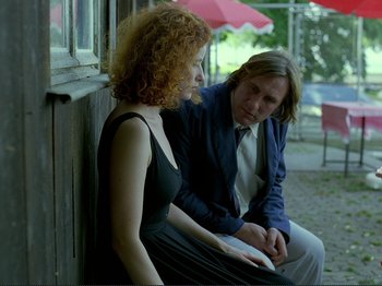Movie still from “Oh, Woe Is Me” (1993), directed by Jean-Luc Godard – A man and a woman sitting next to each other on a porch; Medium shot, Over the shoulder angle