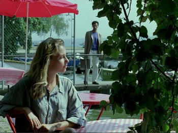 Movie still from “Oh, Woe Is Me” (1993), directed by Jean-Luc Godard – A woman sitting at an outdoor table in front of a man; Medium shot, Over the shoulder angle