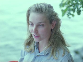 Movie still from “Oh, Woe Is Me” (1993), directed by Jean-Luc Godard – A woman with long blonde hair is smiling for the camera; Close Up shot, Over the shoulder angle
