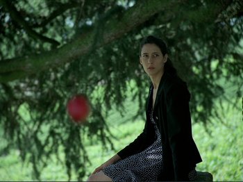 Movie still from “Oh, Woe Is Me” (1993), directed by Jean-Luc Godard – A woman sitting on the ground next to a tree; Medium shot, Low angle