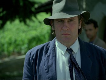 Movie still from “Oh, Woe Is Me” (1993), directed by Jean-Luc Godard – A person wearing a suit and a hat; Close Up shot, Over the shoulder angle