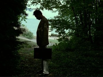 Movie still from “Oh, Woe Is Me” (1993), directed by Jean-Luc Godard – A man standing in the woods holding a briefcase; Wide shot, Low angle