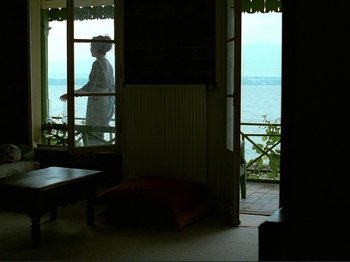 Movie still from “Oh, Woe Is Me” (1993), directed by Jean-Luc Godard – A person standing in a room looking out of a window; Wide shot, Low angle