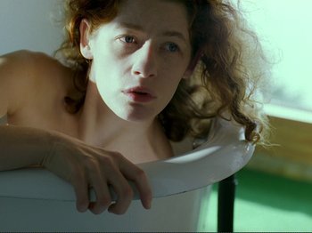Movie still from “Oh, Woe Is Me” (1993), directed by Jean-Luc Godard – A woman with curly red hair leaning on a toilet; Close Up shot, High angle