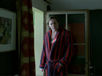Movie still from “Oh, Woe Is Me” (1993), directed by Jean-Luc Godard – A man in a robe standing in front of an open window; Medium shot, Over the shoulder angle