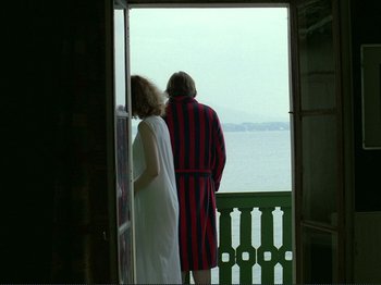 Movie still from “Oh, Woe Is Me” (1993), directed by Jean-Luc Godard – A man and a woman standing at the door of a house; Wide shot, Over the shoulder angle