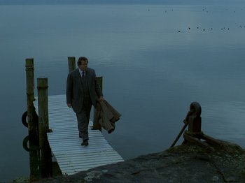 Movie still from “Oh, Woe Is Me” (1993), directed by Jean-Luc Godard – A man in a suit and tie walking across a pier; Wide shot, Over the shoulder angle
