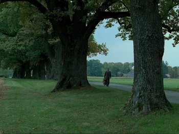Movie still from “Oh, Woe Is Me” (1993), directed by Jean-Luc Godard – A man standing next to a tree on the side of a road; Extreme Wide shot, Low angle