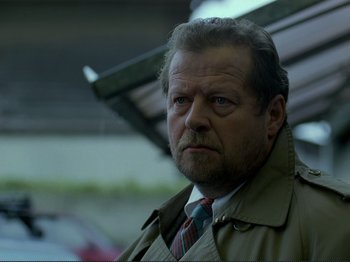 Movie still from “Oh, Woe Is Me” (1993), directed by Jean-Luc Godard – An older man wearing a trench coat and a tie; Close Up shot, Low angle