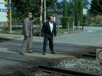 Movie still from “Oh, Woe Is Me” (1993), directed by Jean-Luc Godard – A couple of men standing next to each other on some train tracks; Wide shot, Low angle