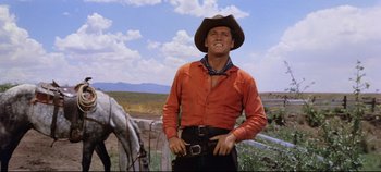 Movie still from “Oklahoma!” (1955), directed by Fred Zinnemann – A man wearing a cowboy hat standing next to a horse; Medium shot, Low angle