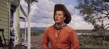 Movie still from “Oklahoma!” (1955), directed by Fred Zinnemann – A man wearing a cowboy hat and a red shirt; Medium shot, Low angle