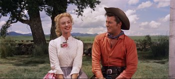 Movie still from “Oklahoma!” (1955), directed by Fred Zinnemann – A man and a woman sitting next to each other on the grass; Medium shot, Low angle