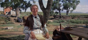 Movie still from “Oklahoma!” (1955), directed by Fred Zinnemann – An older woman sitting on a bench near a tree; Medium shot, Low angle