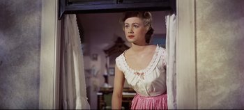 Movie still from “Oklahoma!” (1955), directed by Fred Zinnemann – A woman standing in front of a window with curtains open; Medium shot, Low angle