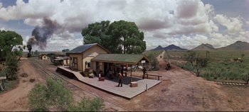 Movie still from “Oklahoma!” (1955), directed by Fred Zinnemann – An old western style building with people standing on the ground; Extreme Wide shot, Low angle