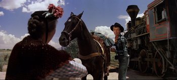 Movie still from “Oklahoma!” (1955), directed by Fred Zinnemann – A man standing next to a horse on a dirt road; Medium shot, Low angle