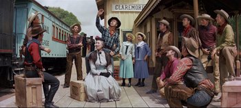 Movie still from “Oklahoma!” (1955), directed by Fred Zinnemann – A group of men and women standing on a street; Wide shot, Low angle