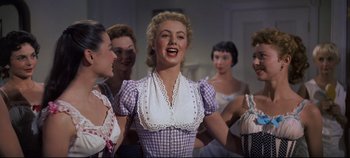 Movie still from “Oklahoma!” (1955), directed by Fred Zinnemann – A group of women standing next to each other in a room; Medium shot, Low angle