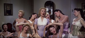 Movie still from “Oklahoma!” (1955), directed by Fred Zinnemann – A woman surrounded by a group of women; Medium shot, Low angle