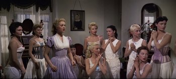 Movie still from “Oklahoma!” (1955), directed by Fred Zinnemann – A group of women standing next to each other in a room; Medium shot, Low angle