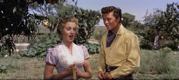 Movie still from “Oklahoma!” (1955), directed by Fred Zinnemann – A man and a woman standing next to each other in a field; Medium shot, Low angle