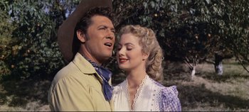 Movie still from “Oklahoma!” (1955), directed by Fred Zinnemann – A man and a woman standing next to each other; Medium shot, Low angle