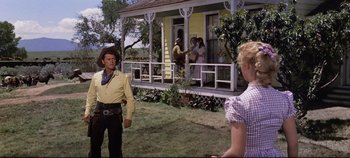 Movie still from “Oklahoma!” (1955), directed by Fred Zinnemann – A man and a woman standing in front of a house; Wide shot, Low angle