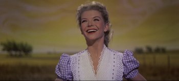 Movie still from “Oklahoma!” (1955), directed by Fred Zinnemann – A woman in a purple and white dress smiling; Close Up shot, Low angle