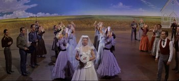 Movie still from “Oklahoma!” (1955), directed by Fred Zinnemann – A woman in a wedding dress surrounded by a group of women; Wide shot, Low angle