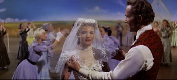 Movie still from “Oklahoma!” (1955), directed by Fred Zinnemann – A woman wearing a wedding veil standing next to a man; Medium shot, Low angle