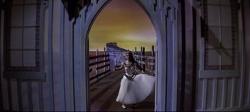 Movie still from “Oklahoma!” (1955), directed by Fred Zinnemann – A woman in a white dress standing on a bridge; Wide shot, Low angle