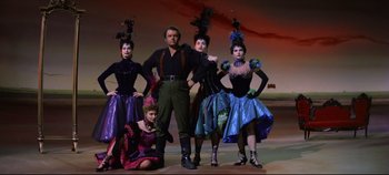 Movie still from “Oklahoma!” (1955), directed by Fred Zinnemann – A group of people standing next to each other on a stage; Wide shot, Low angle