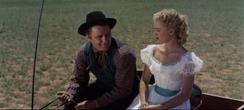 Movie still from “Oklahoma!” (1955), directed by Fred Zinnemann – A man and a woman sitting next to each other on the grass; Medium shot, Low angle