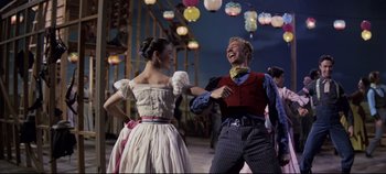 Movie still from “Oklahoma!” (1955), directed by Fred Zinnemann – A man and a woman are dancing in front of lights; Medium shot, Low angle
