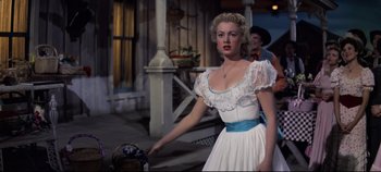 Movie still from “Oklahoma!” (1955), directed by Fred Zinnemann – A woman in a white dress standing on a porch; Medium shot, Low angle