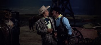 Movie still from “Oklahoma!” (1955), directed by Fred Zinnemann – Two men in cowboy hats and suits talking to each other; Medium shot, Over the shoulder angle