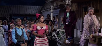 Movie still from “Oklahoma!” (1955), directed by Fred Zinnemann – A woman standing next to an older man in front of a group of people; Medium shot, Low angle