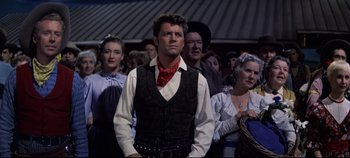 Movie still from “Oklahoma!” (1955), directed by Fred Zinnemann – A group of people standing in front of each other; Medium shot, Over the shoulder angle