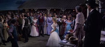 Movie still from “Oklahoma!” (1955), directed by Fred Zinnemann – A group of people standing around a crowd of people; Wide shot, Over the shoulder angle