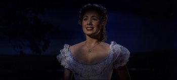 Movie still from “Oklahoma!” (1955), directed by Fred Zinnemann – A woman in a white dress smiling for the camera; Close Up shot, Over the shoulder angle
