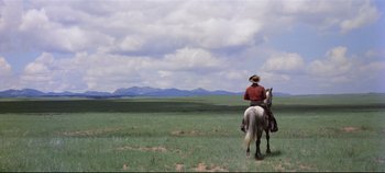 Movie still from “Oklahoma!” (1955), directed by Fred Zinnemann – A man riding a horse in a field with mountains in the background; Extreme Wide shot, Low angle