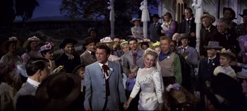 Movie still from “Oklahoma!” (1955), directed by Fred Zinnemann – A man and a woman are holding hands in front of a crowd of onlookers; Medium shot, High angle