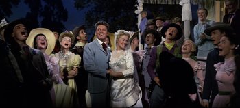 Movie still from “Oklahoma!” (1955), directed by Fred Zinnemann – A man and a woman standing next to each other in front of a group of people; Medium shot, Low angle