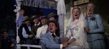 Movie still from “Oklahoma!” (1955), directed by Fred Zinnemann – A group of people sitting next to each other on a porch; Medium shot, Low angle
